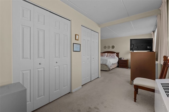 bedroom featuring light colored carpet and multiple closets