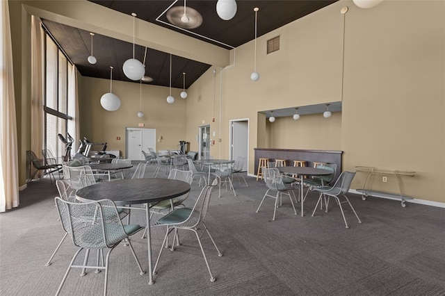 dining space featuring carpet floors, visible vents, a towering ceiling, and baseboards