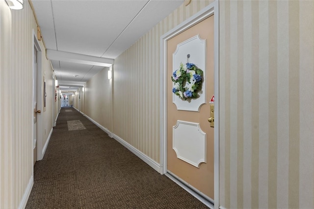 hall featuring wallpapered walls, attic access, baseboards, and dark carpet