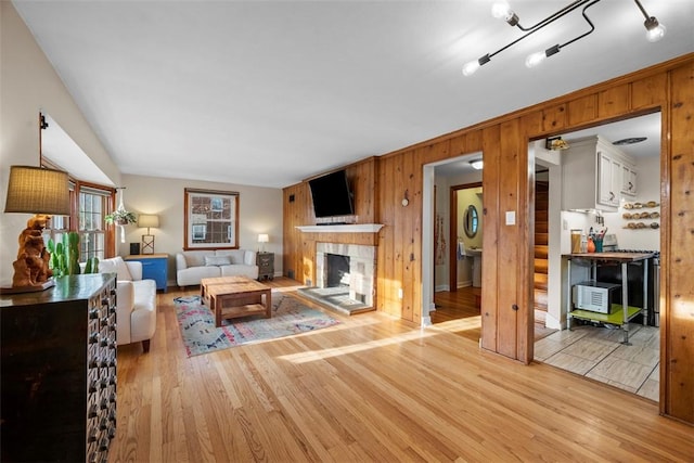 living area featuring a fireplace with raised hearth, wood walls, and light wood finished floors