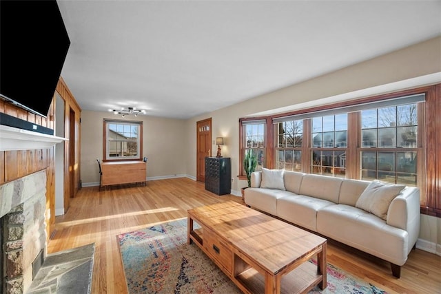 living area featuring plenty of natural light, a fireplace, baseboards, and light wood-style floors