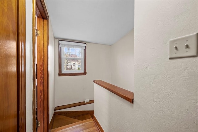 staircase with a textured wall, baseboards, and wood finished floors