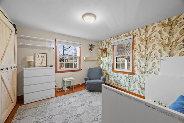 unfurnished room with wallpapered walls, a barn door, baseboards, radiator heating unit, and wood finished floors