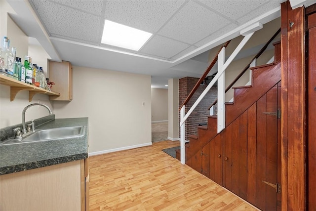 kitchen with a drop ceiling, a sink, baseboards, light wood finished floors, and dark countertops