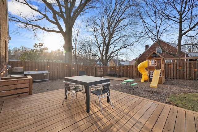 wooden deck with a fenced backyard, a playground, and outdoor dining space