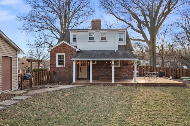 back of property with brick siding, a chimney, fence, and a lawn