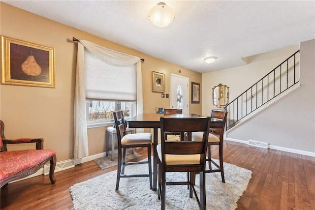 dining area featuring stairway, wood-type flooring, visible vents, and baseboards