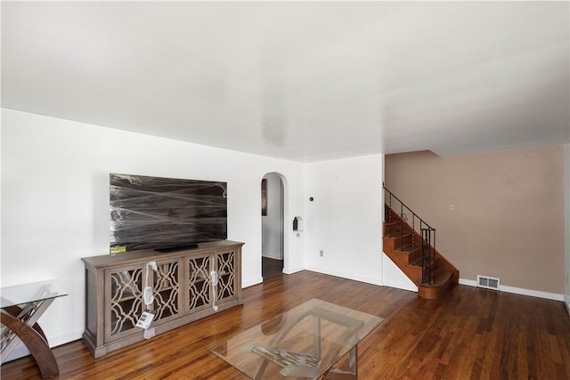 living room featuring arched walkways, wood finished floors, visible vents, baseboards, and stairs