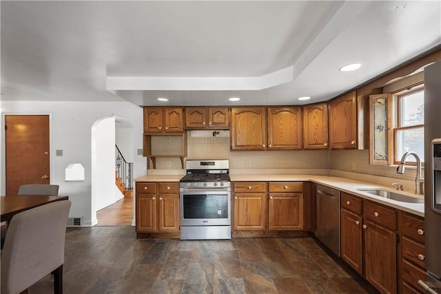 kitchen featuring a sink, light countertops, appliances with stainless steel finishes, backsplash, and brown cabinets