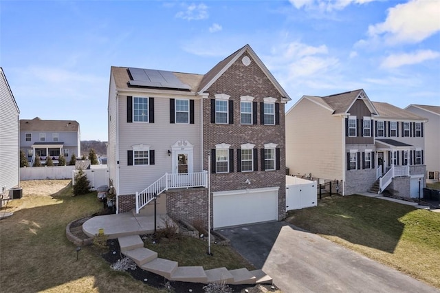 view of front of property featuring solar panels, aphalt driveway, fence, and brick siding