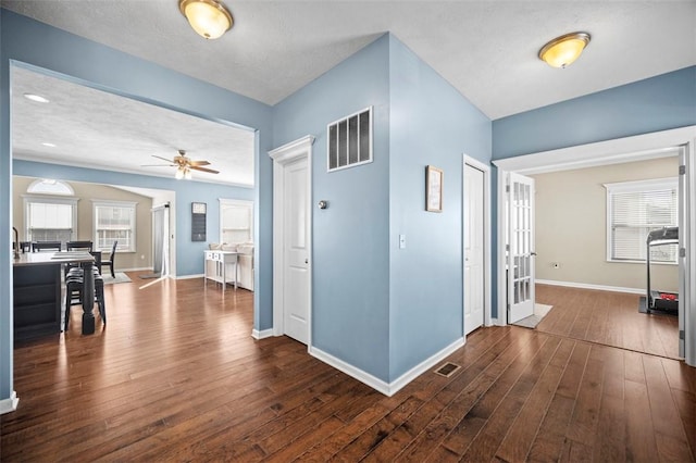 corridor with baseboards, visible vents, dark wood finished floors, and a wealth of natural light