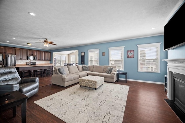 living room with a fireplace with flush hearth, dark wood-type flooring, ornamental molding, and baseboards