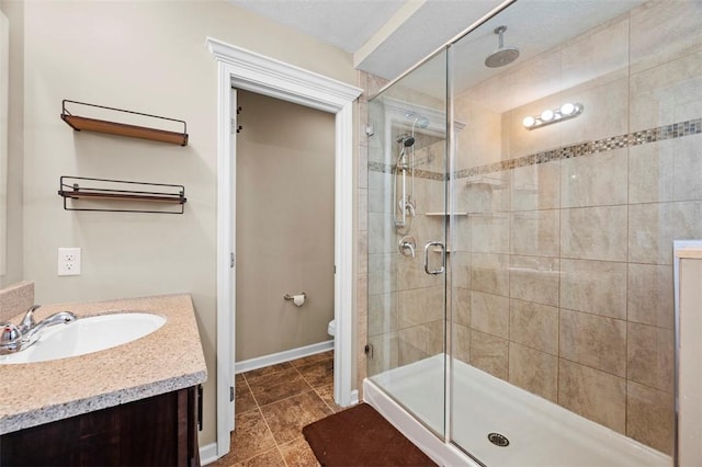 bathroom featuring baseboards, a shower stall, toilet, and vanity