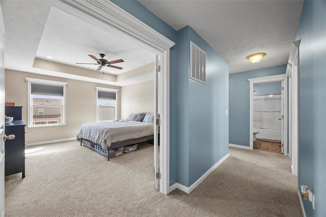 carpeted bedroom with baseboards, visible vents, a raised ceiling, and ensuite bathroom