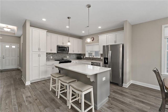 kitchen featuring dark wood-style floors, decorative backsplash, appliances with stainless steel finishes, white cabinetry, and a sink