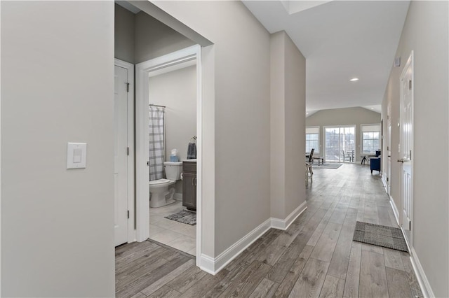 hallway featuring lofted ceiling, baseboards, and wood finished floors