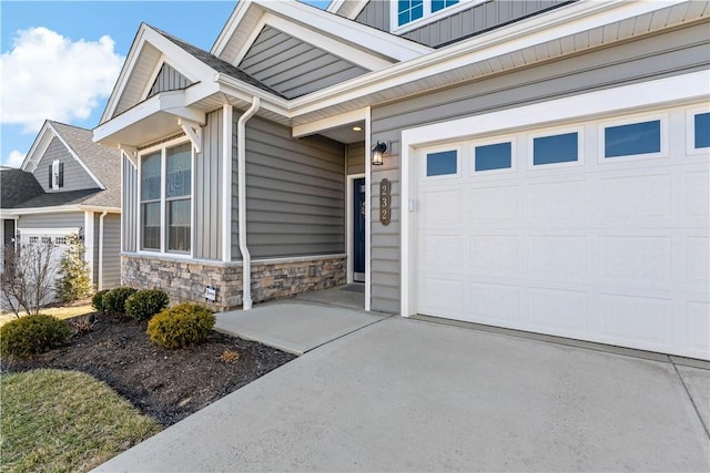 entrance to property with board and batten siding, stone siding, an attached garage, and concrete driveway