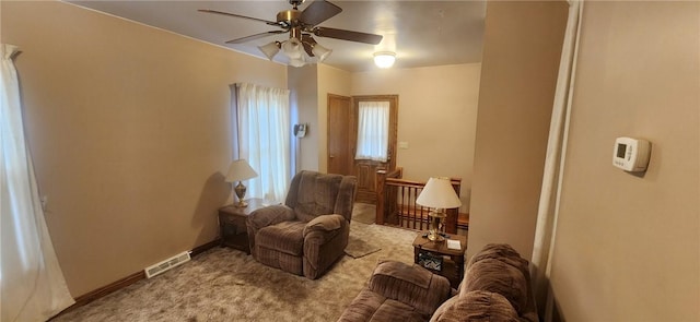 living area featuring visible vents, a ceiling fan, carpet flooring, an upstairs landing, and baseboards