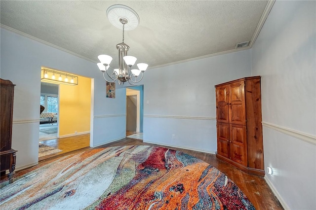 unfurnished room featuring a textured ceiling, a notable chandelier, wood finished floors, and crown molding