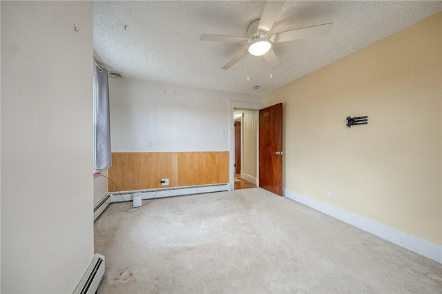 carpeted empty room with a textured ceiling, wooden walls, a wainscoted wall, a ceiling fan, and visible vents