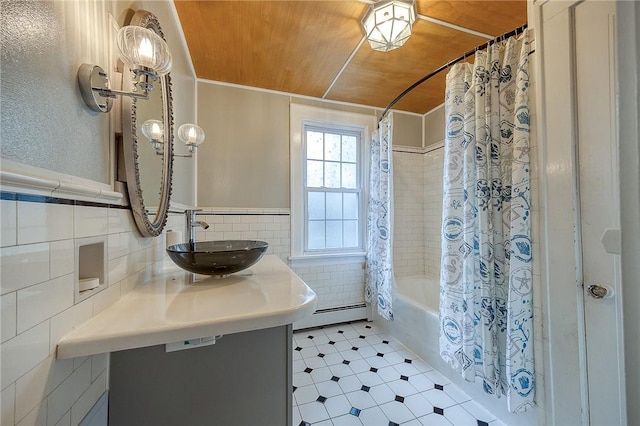 bathroom with tile patterned floors, shower / bath combo with shower curtain, baseboard heating, vanity, and tile walls