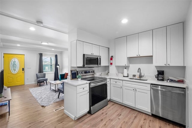 kitchen with appliances with stainless steel finishes, light wood-type flooring, light countertops, and a sink