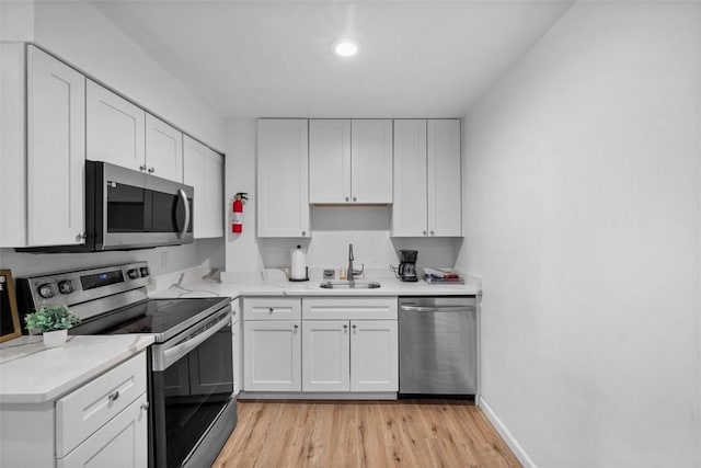 kitchen with stainless steel appliances, light wood-style flooring, white cabinets, a sink, and baseboards