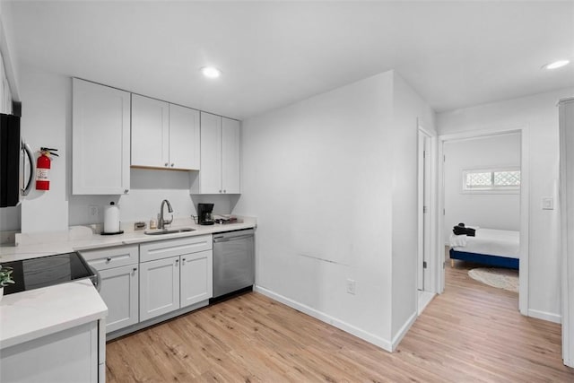 kitchen with light countertops, light wood-style flooring, white cabinetry, a sink, and dishwasher