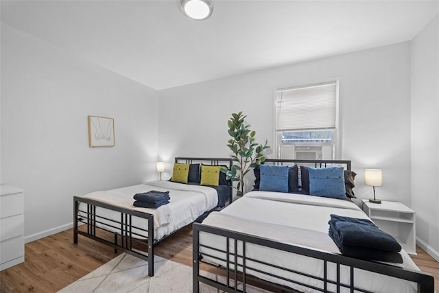 bedroom with cooling unit, baseboards, and wood finished floors