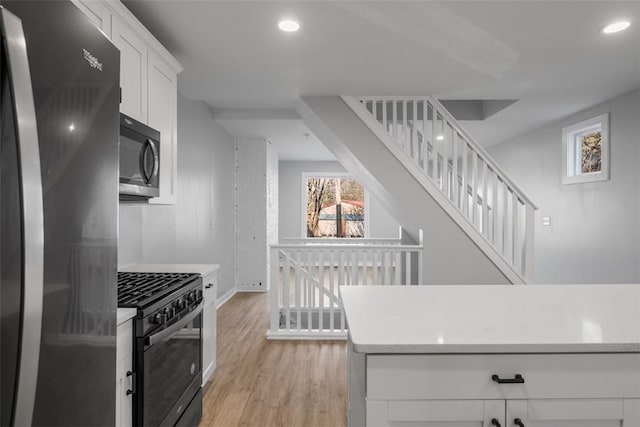 kitchen with light wood finished floors, refrigerator, black range with gas stovetop, light countertops, and white cabinetry