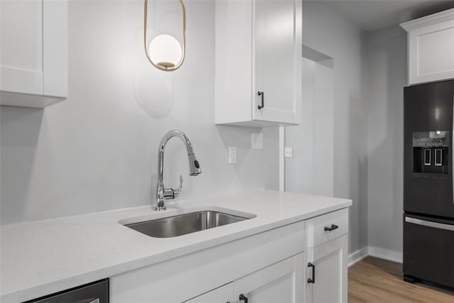 kitchen with light wood-style floors, white cabinetry, a sink, and black fridge