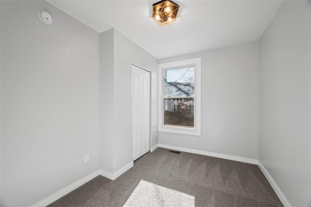 empty room featuring visible vents, dark carpet, and baseboards