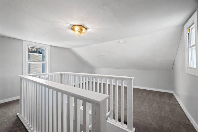 hall featuring lofted ceiling, dark carpet, and baseboards