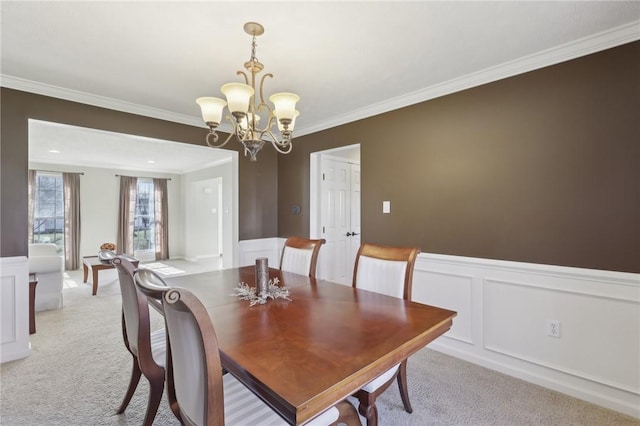 dining space with light carpet, a wainscoted wall, ornamental molding, and a notable chandelier