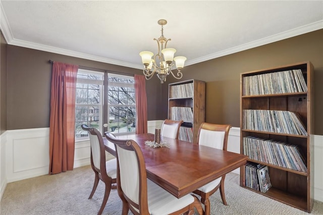 dining space with light carpet, a chandelier, ornamental molding, and wainscoting