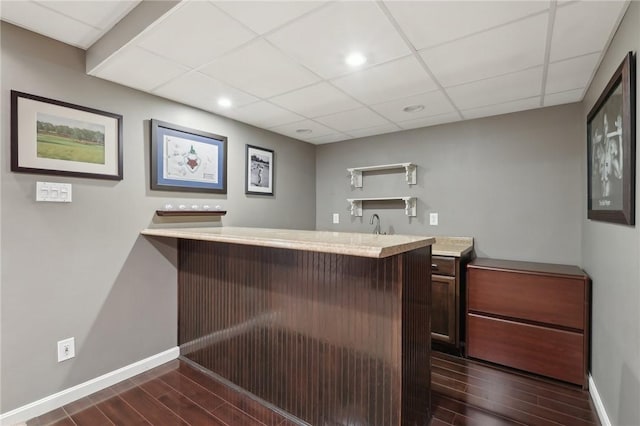 bar featuring wet bar, baseboards, a drop ceiling, and dark wood-style flooring