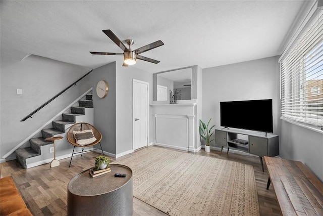 living room featuring a textured ceiling, wood finished floors, a ceiling fan, baseboards, and stairway