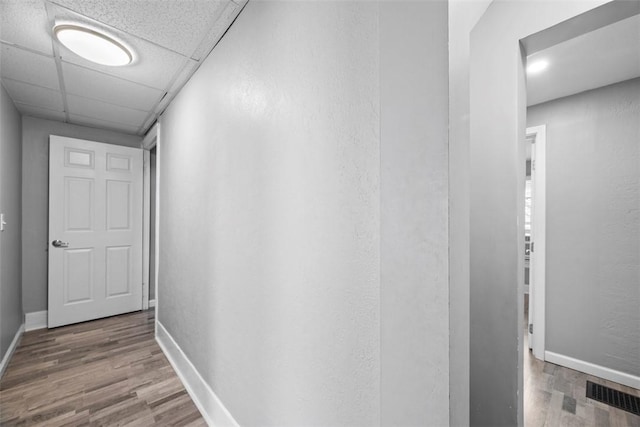 hall featuring a paneled ceiling, wood finished floors, visible vents, and baseboards