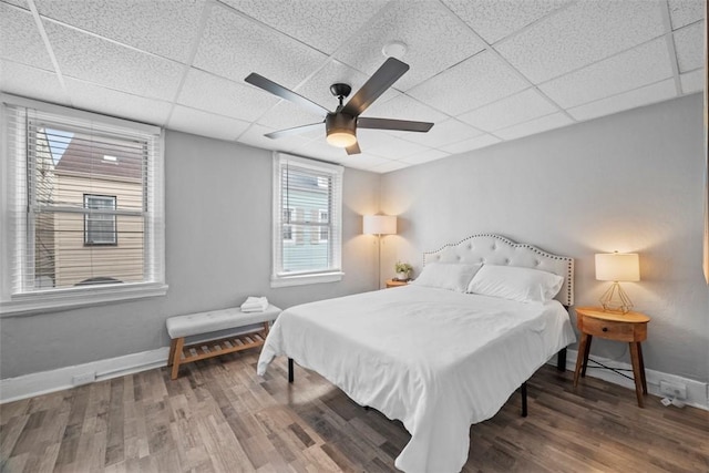 bedroom featuring a drop ceiling, ceiling fan, baseboards, and wood finished floors