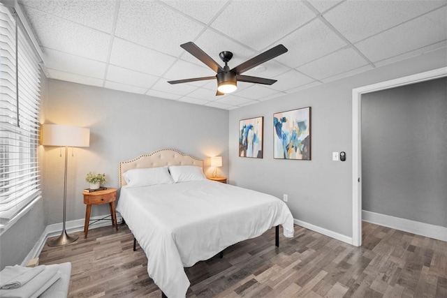 bedroom with a paneled ceiling, a ceiling fan, baseboards, and wood finished floors