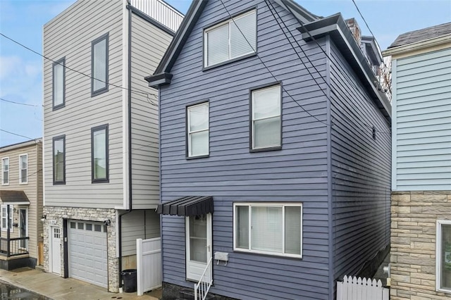 exterior space featuring an attached garage, stone siding, and fence