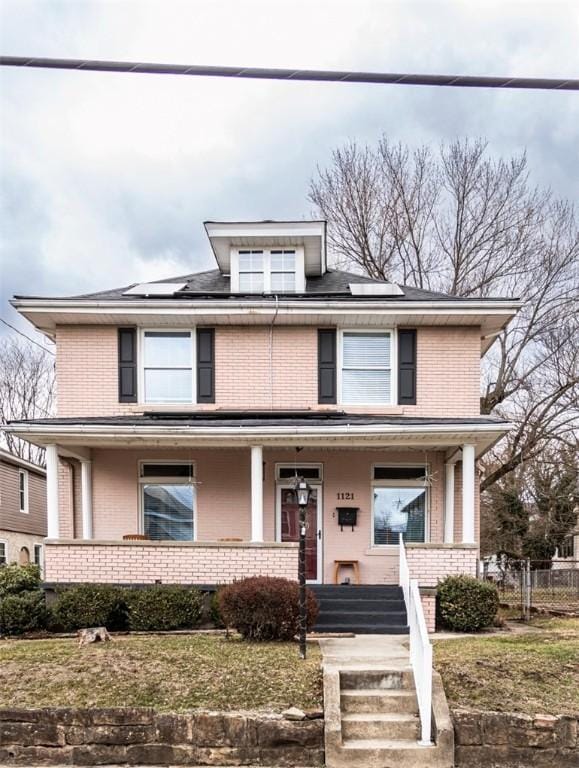 american foursquare style home with a porch, brick siding, and solar panels