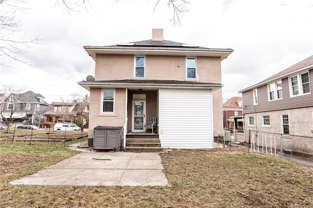 back of house featuring solar panels, brick siding, a chimney, and a fenced backyard