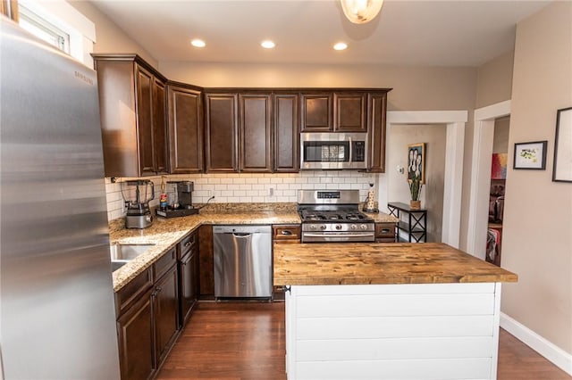 kitchen featuring backsplash, butcher block counters, stainless steel appliances, and dark brown cabinets