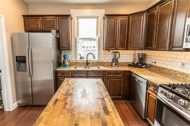 kitchen featuring butcher block counters, dark wood-type flooring, a sink, appliances with stainless steel finishes, and decorative backsplash