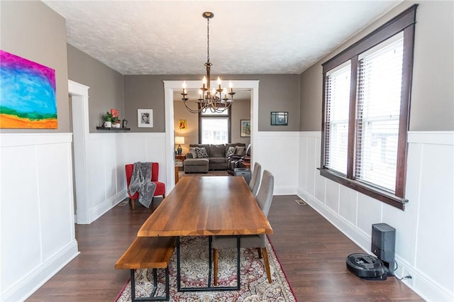 dining space with a wainscoted wall, a textured ceiling, dark wood-style floors, and an inviting chandelier