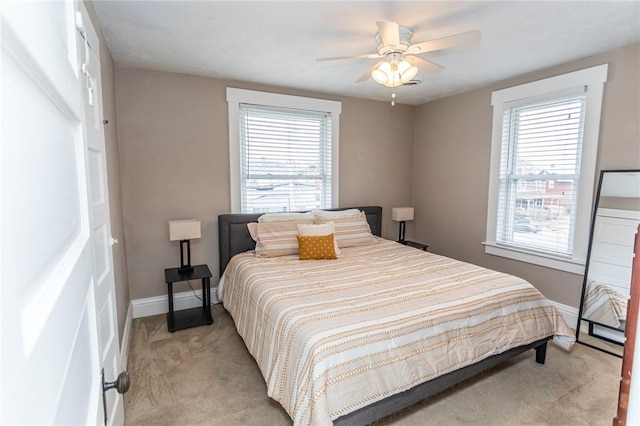 bedroom with a ceiling fan, light colored carpet, baseboards, and multiple windows