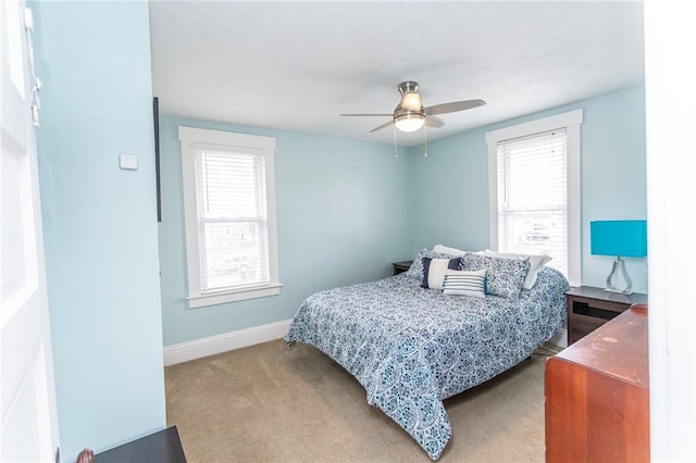 bedroom featuring light carpet, ceiling fan, multiple windows, and baseboards