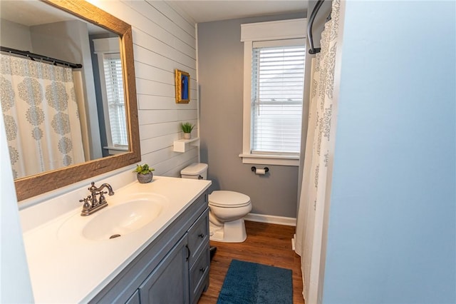 bathroom featuring toilet, wood finished floors, vanity, and wooden walls