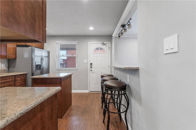 kitchen featuring baseboards, stainless steel fridge with ice dispenser, a kitchen breakfast bar, dark wood-type flooring, and a center island